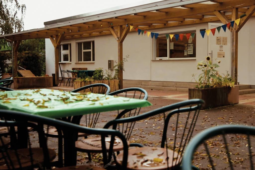 Außenbereich Emils Ecke: Blick auf Tische und Stühle mit Herbstlaub, im Hintergrund das Gebäude