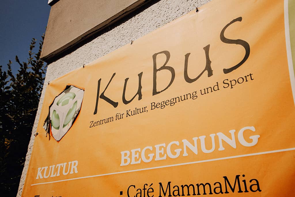 Nahaufnahme: Oranges Banner an Hauswand mit Schriftzug „Kubus – Zentrum für Kultur, Begegnung und Sport”